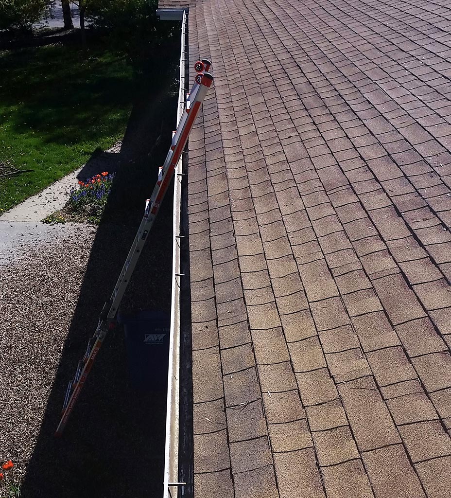 Clear Choice: An extendable ladder leaning against a house roof with shingles, viewed from above on a sunny day, ideal for gutter cleaning.