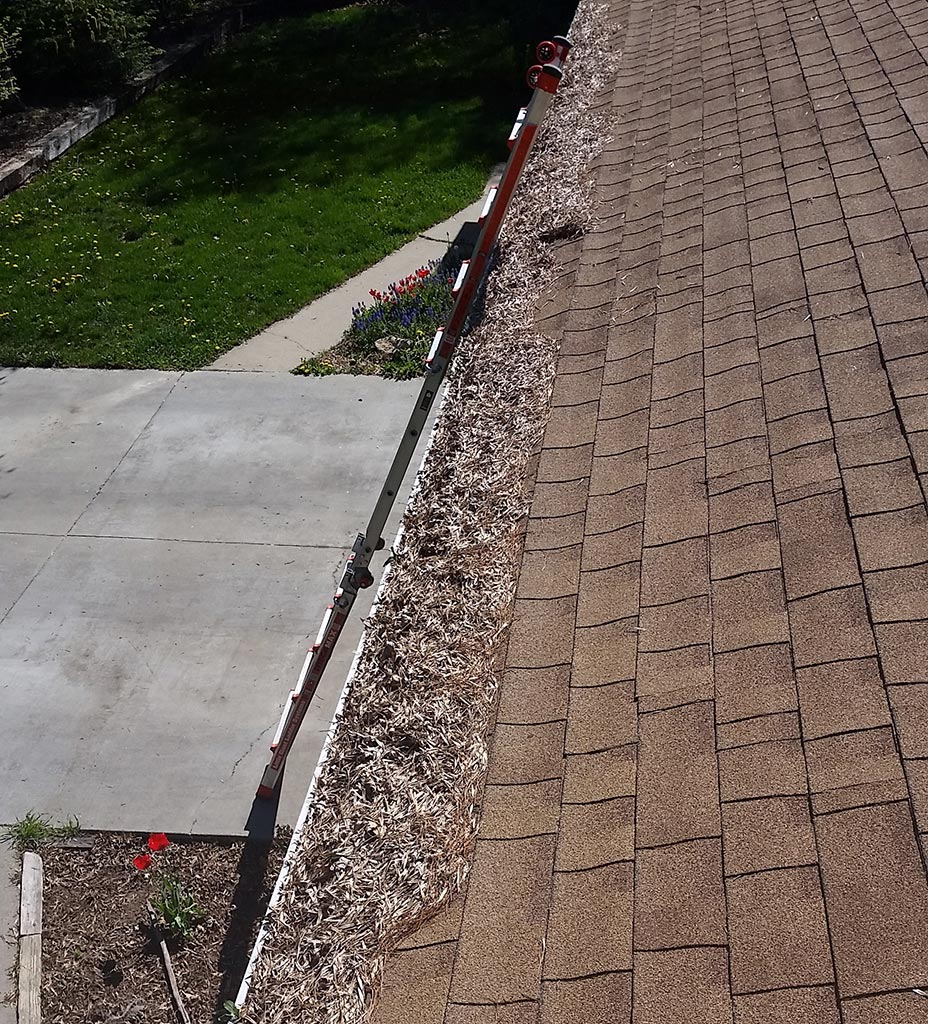 Clear Choice: View from a rooftop showing a gutter filled with leaves, extending along the edge, with a neatly trimmed lawn and a pathway below in Boise Valley.