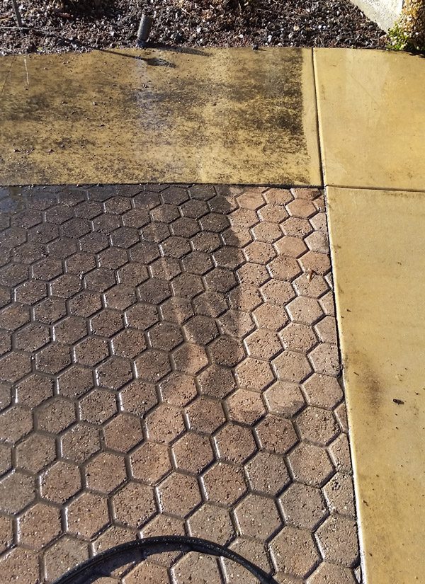 Clear Choice: A sidewalk displaying a transition from wet concrete to dry, patterned paving, with the shadow of a person visible across the scene after power washing.