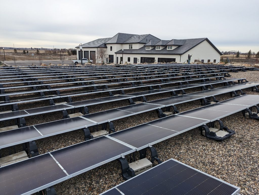 Clear Choice: Rows of solar panels in front of a large modern house with a grey roof, located in Boise Valley under a cloudy sky.