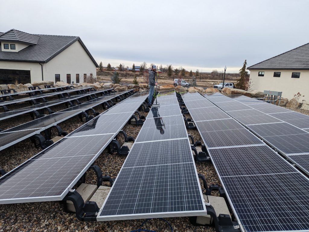 Clear Choice: Worker cleaning solar panels at a large outdoor solar farm with residential houses nearby under an overcast sky in the Boise Valley.