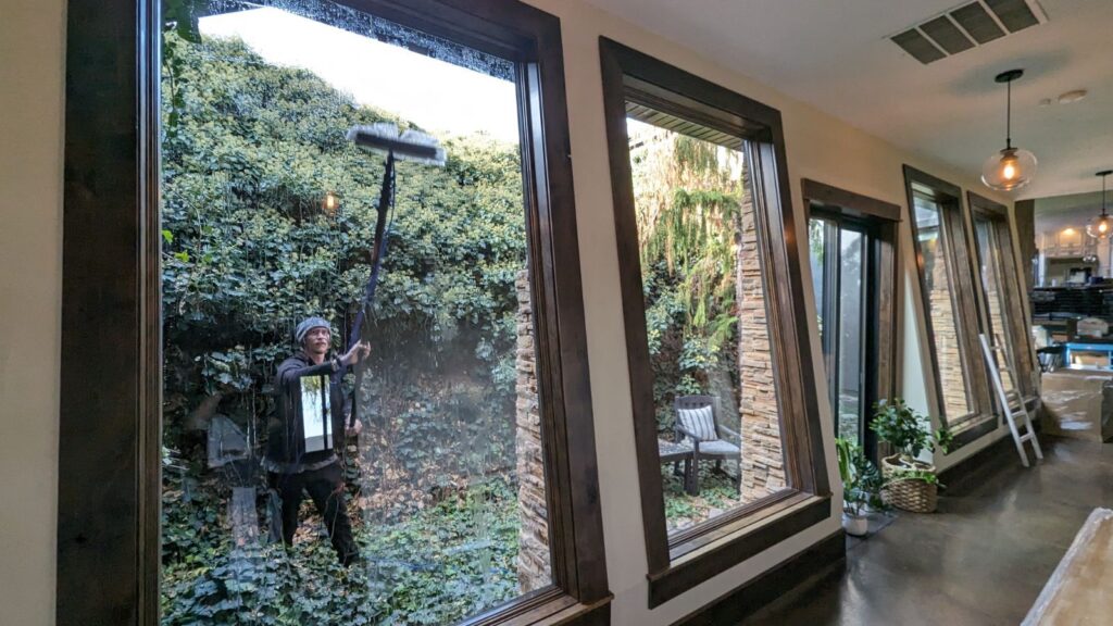 Clear Choice: A person cleaning floor-to-ceiling windows using a squeegee, with a lush vertical garden visible outside.