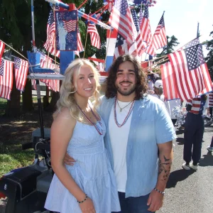 Clear Choice: A smiling couple stands together at an outdoor event decorated with numerous American flags. Both are casually dressed and wearing beaded necklaces.