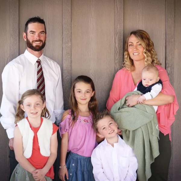Clear Choice: A family of six poses together, including a man, woman, three young girls, and a baby held by the woman, standing against a wooden wall.