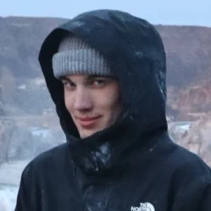 Clear Choice: A person wearing a gray knit beanie and a black hooded North Face jacket stands outdoors, looking slightly to the side with rocky terrain in the background.