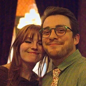 Clear Choice: Two people are standing close together and smiling at the camera indoors, with warm lighting in the background.