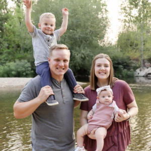 Clear Choice: A family of four by a river, with a man carrying a smiling toddler on his shoulders and a woman holding a baby, who is wearing a headband. Trees and water are in the background.