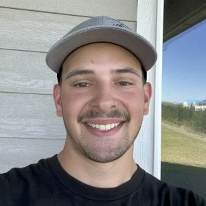 Clear Choice: A young man wearing a gray cap and black shirt smiles at the camera in front of a light-colored exterior wall and a window reflecting a grassy yard.